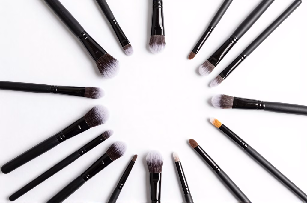 Pinceaux de maquillage professionnels et cosmétiques disposés en flatlay sur fond blanc